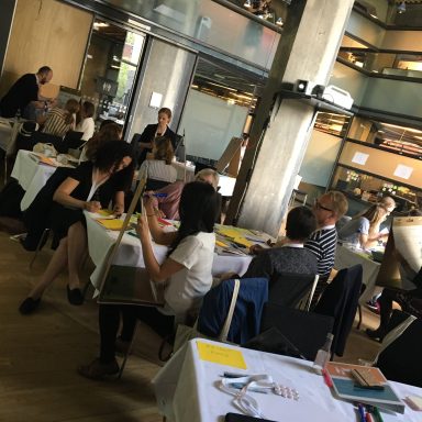 10-15 people in a workshop setting listening to one person describe their poster.