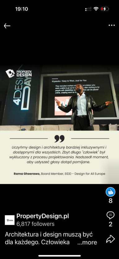 A speaker presenting in front of an audience, gestures towards a screen display.